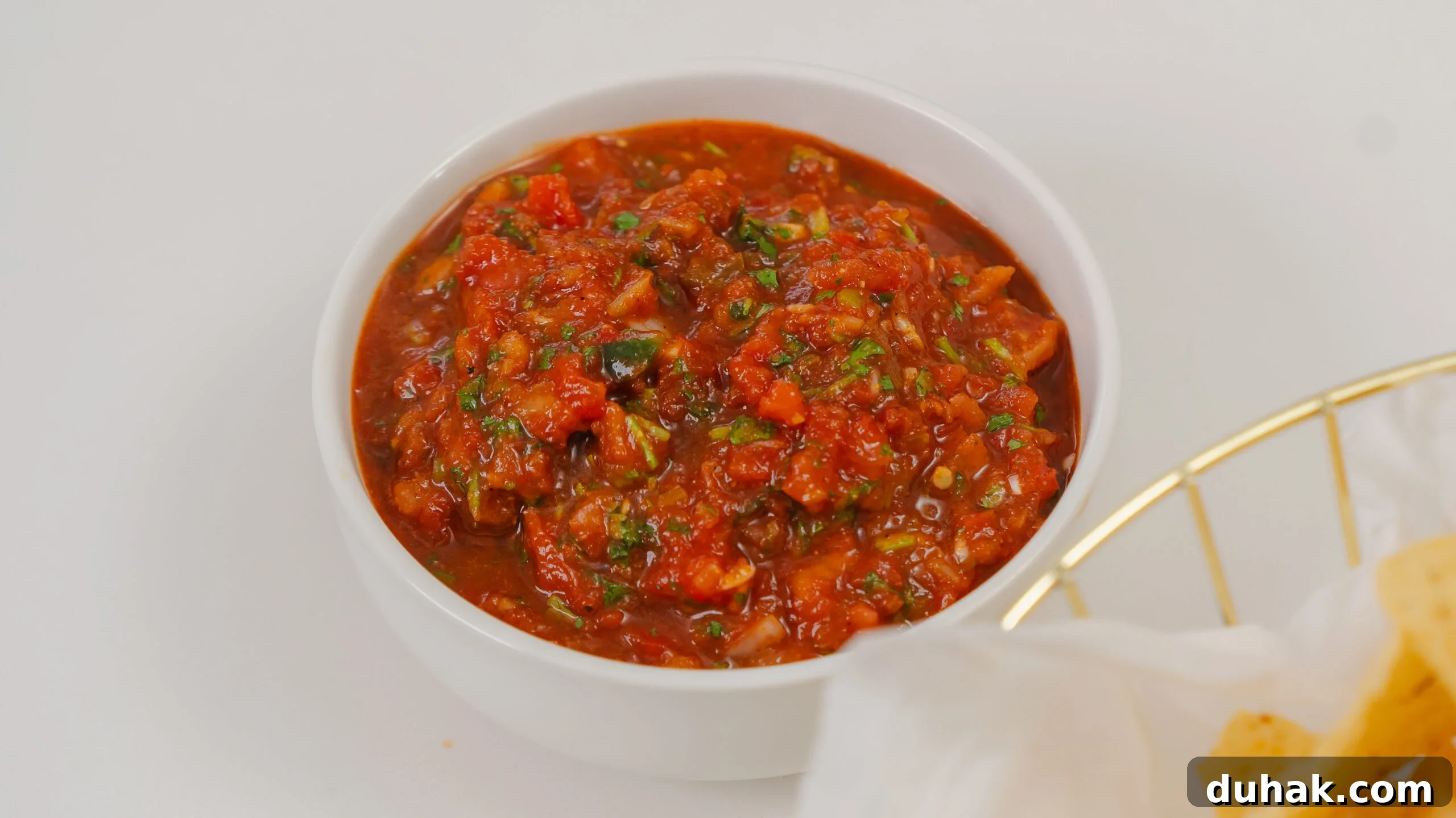 Homemade salsa in a white bowl with nacho chips nearby.