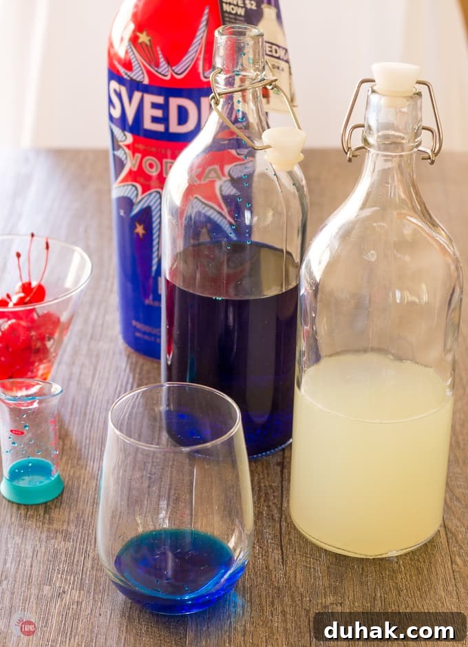 A cocktail glass with blue curacao in it, a bottle of blue liquor, a bottle of white limeade and a bottle of vodka on a wood table
