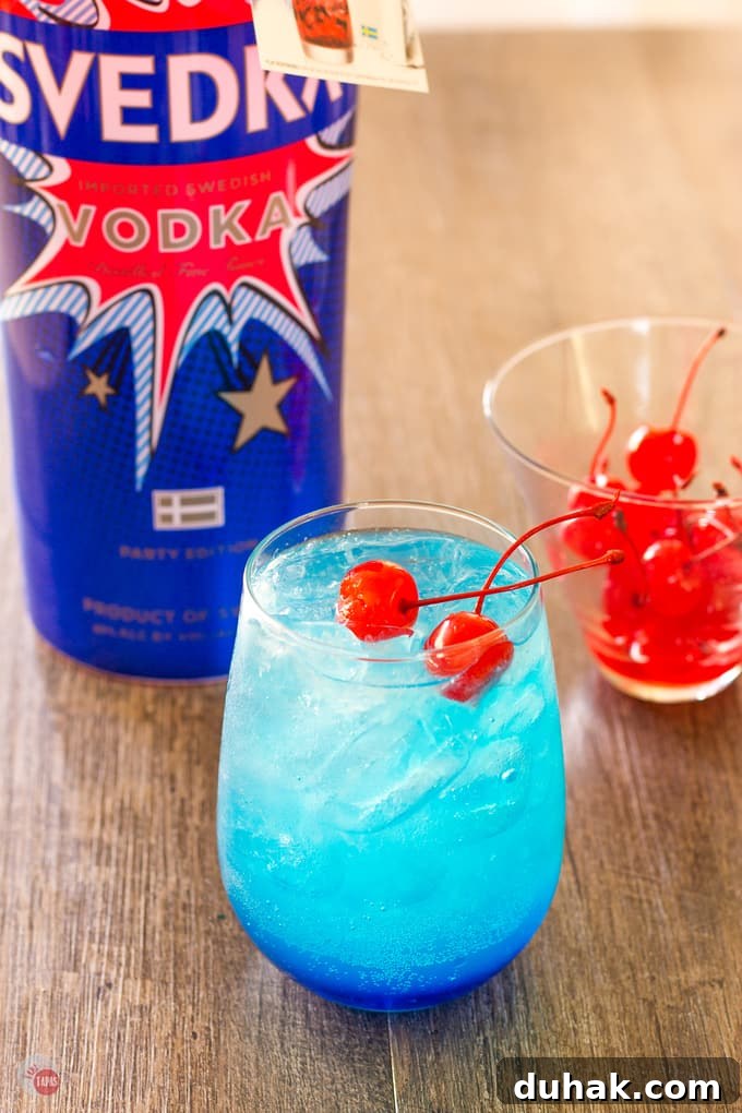 Maraschino cherries in a small cup and on top of the Astro Pop Cocktail. with a bottle of vodka in the background