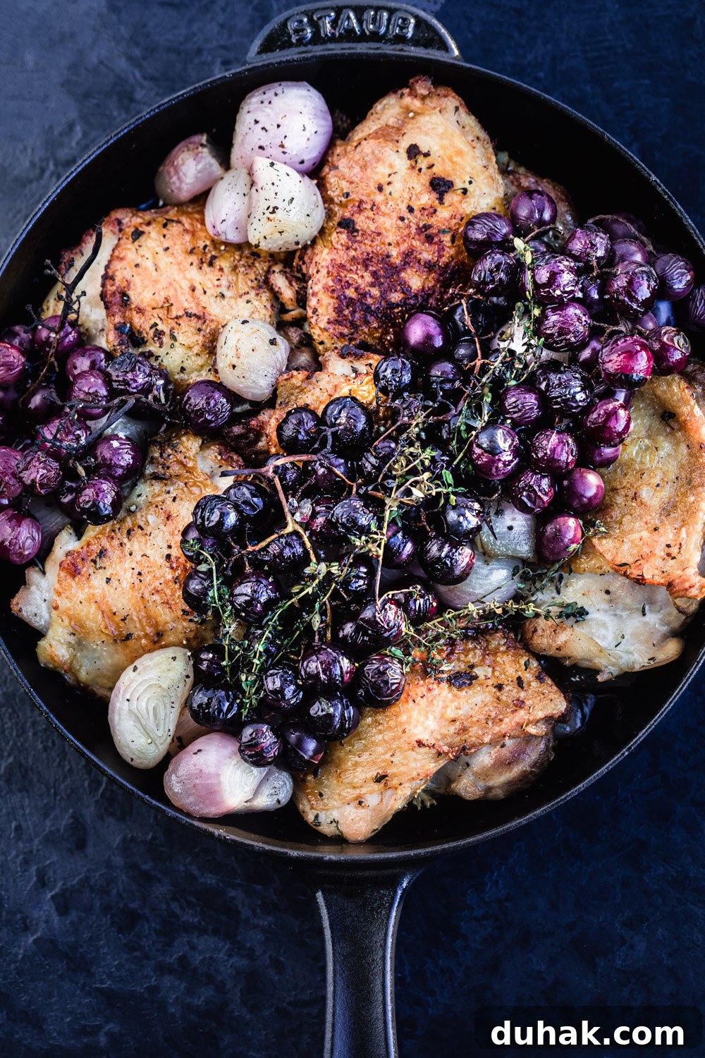 Close up shot of the finished thyme roasted chicken with shallots and grapes, in a cast iron skillet.
