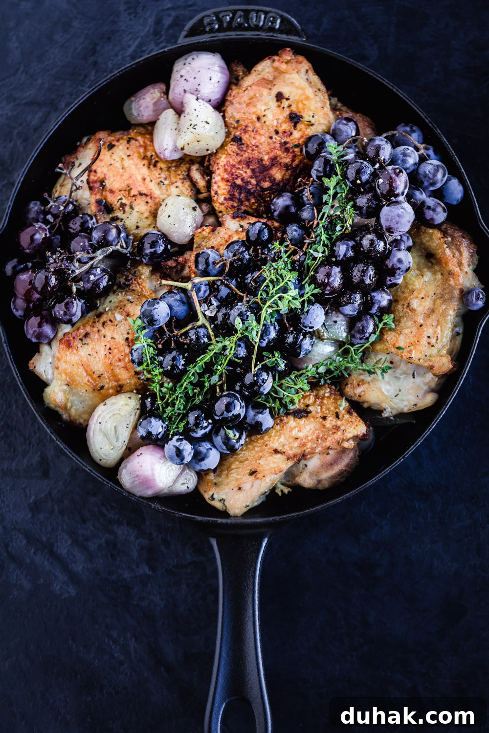 Overhead shot of the thyme roasted chicken with shallots, fresh grapes and thyme about to go back into the oven.