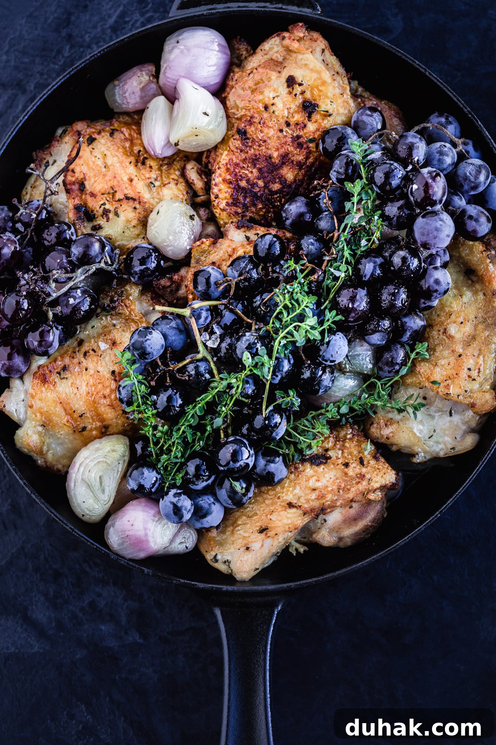 Thyme roasted chicken, about to go into the oven, topped with a bunch of fresh grapes and shallots, overhead shot.
