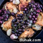 Close up shot of the finished thyme roasted chicken with shallots and grapes, in a cast iron skillet.