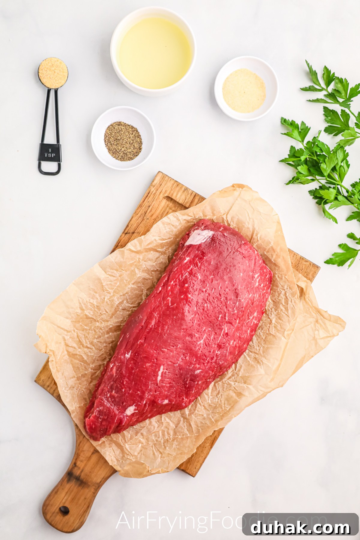 London broil steak and seasonings on a white table.