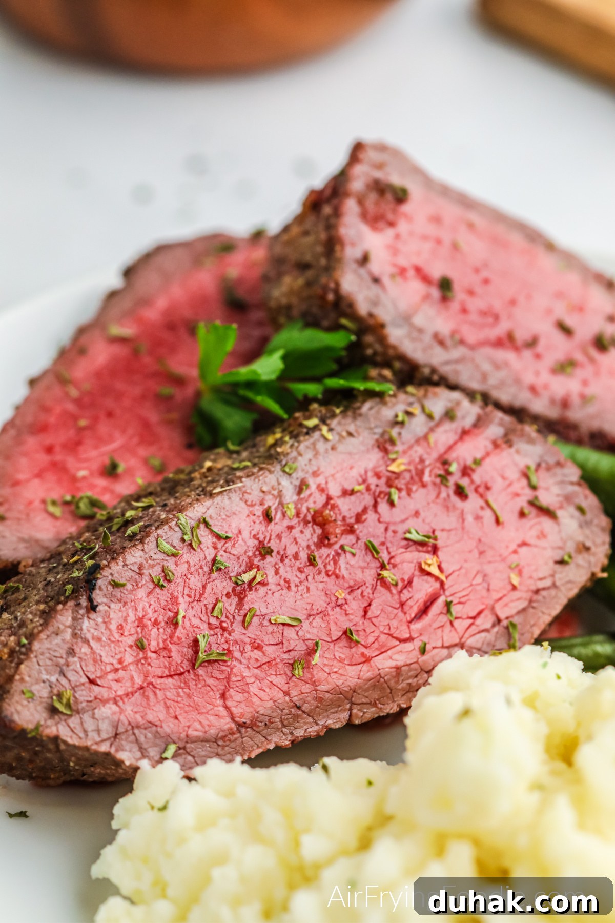 Close up of sliced Air Fryer London Broil on a plate with green beans and mashed potatoes.