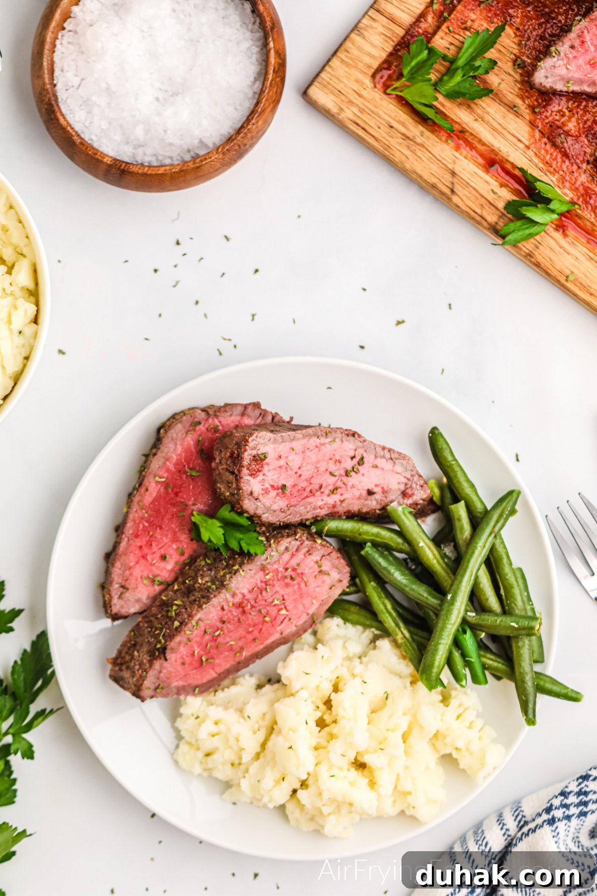 Seasoned London Broil made in the air fryer, served on a white plate with green beans and mashed potatoes.