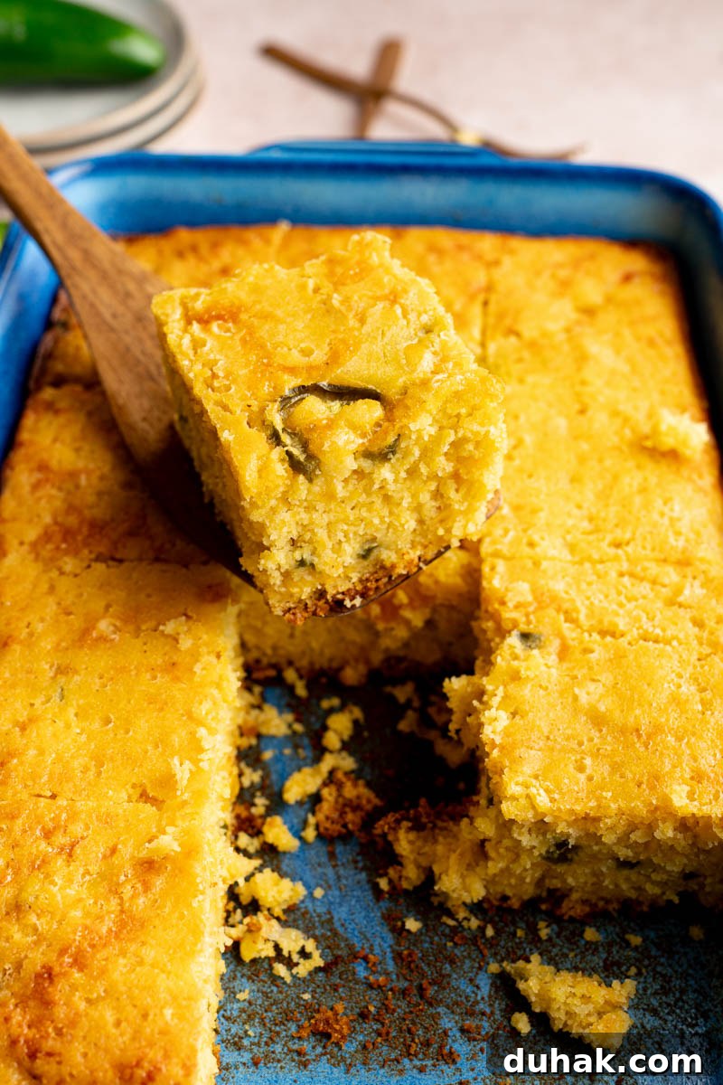 A serving utensil picks up a piece of the jalapeno cheddar cornbread from the baking dish for serving.