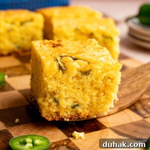 A serving utensil holds a piece of jalapeno cheddar cornbread on top of a wooden cutting board for serving.
