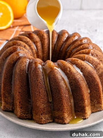 Whole ornage bundt cake being glazed with caramel. White background. Fresh oranges.