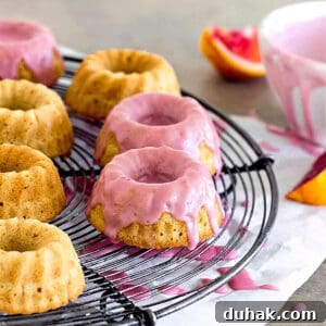Pink glazed mini bundt cakes on a wire rack. White bowl, gray surface, white paper.