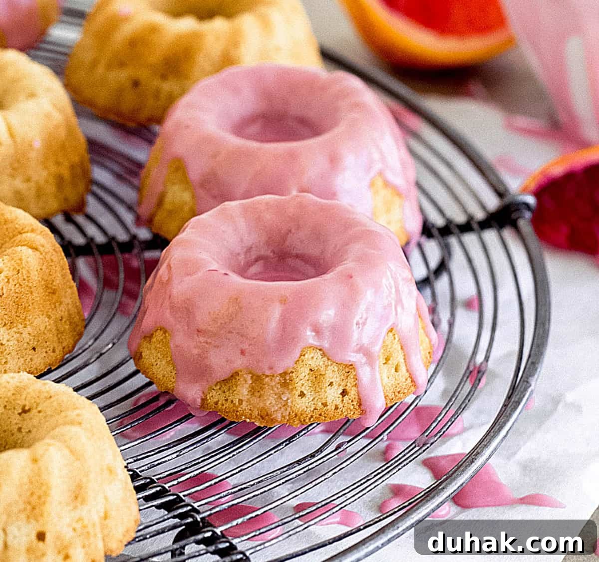Close-up of mini cake with pink glaze on a round grey wire rack