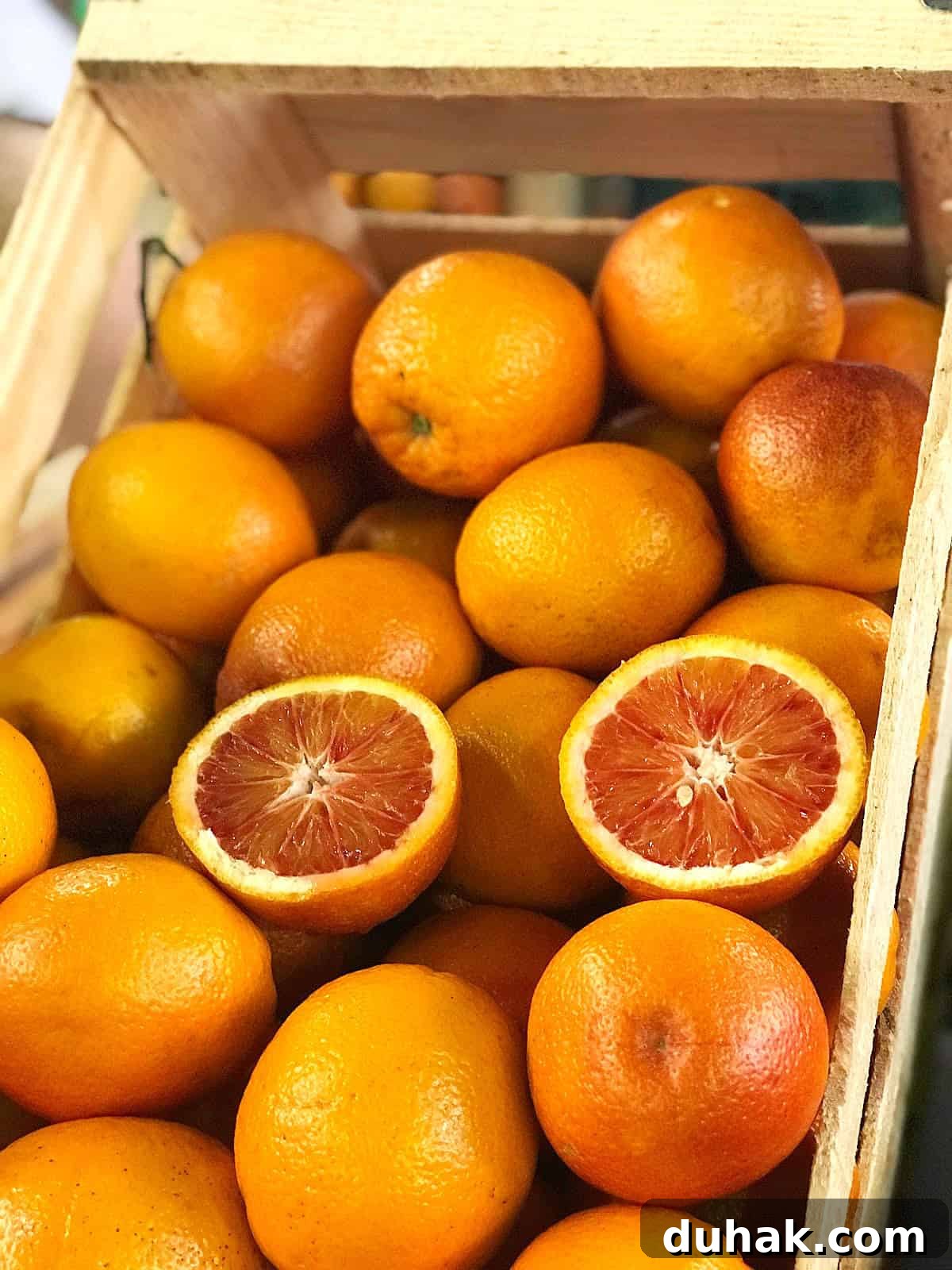 A wooden crate of blood oranges. One is halved.