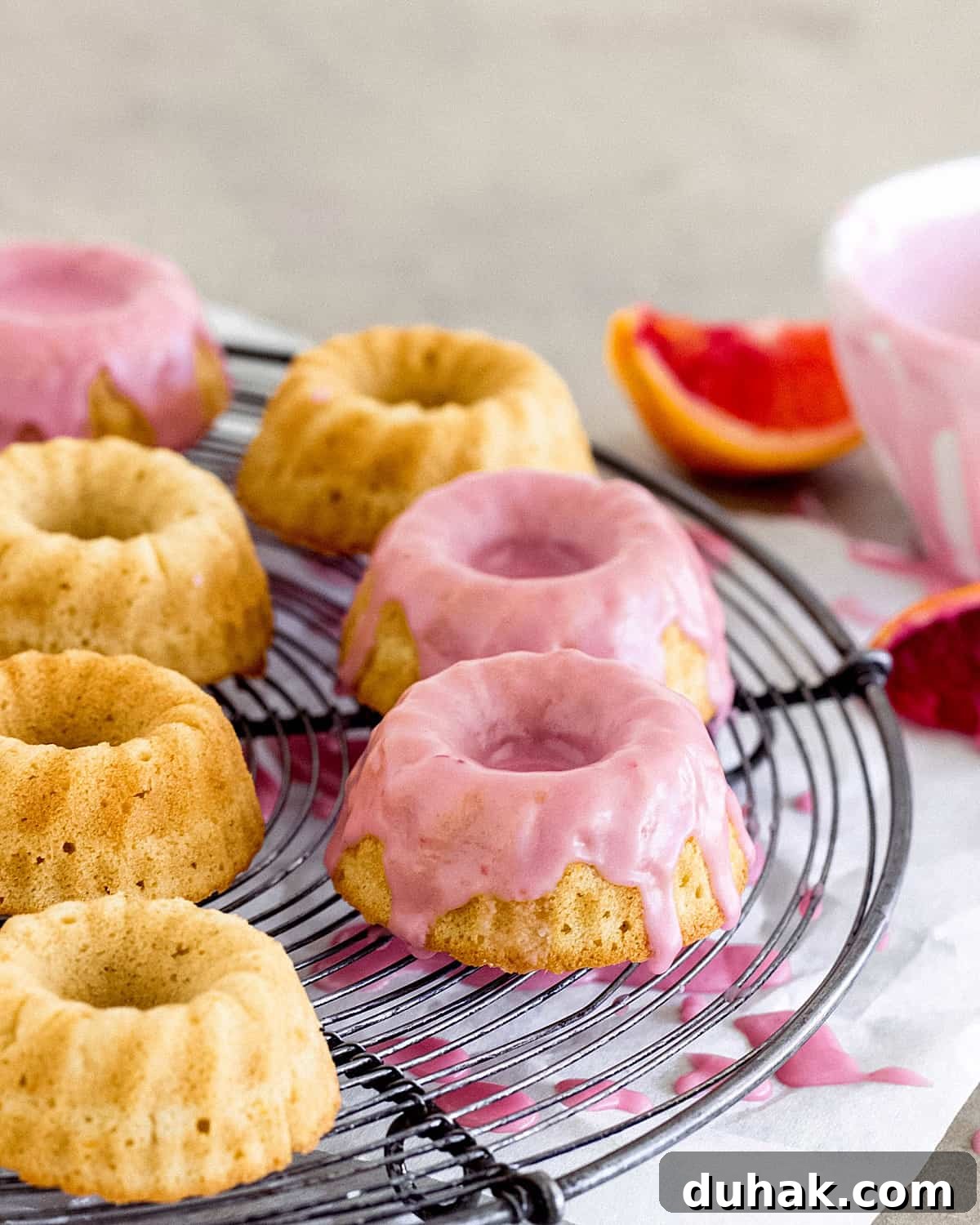 Mini cakes on wire rack with pink glaze, blood orange wedges beside