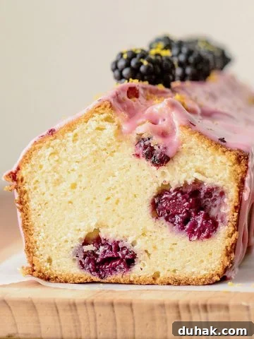 Cut glazed blackberry bread on wooden board, beige background.