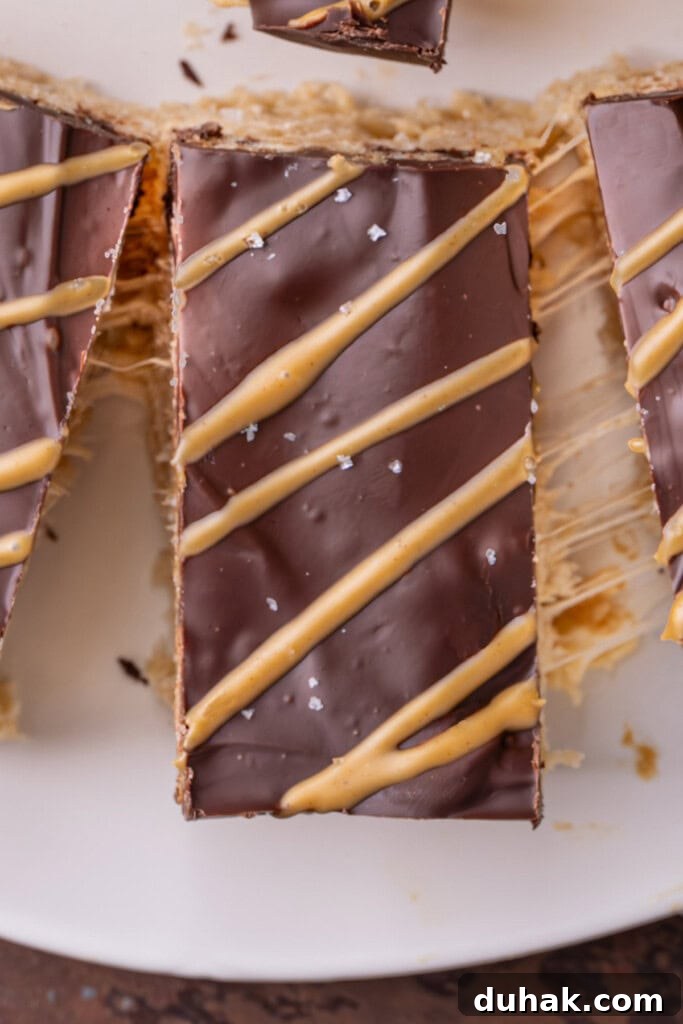 Close up of a peanut butter rice krispie treat covered in chocolate, drizzled with peanut butter and topped with flaky sea salt. 