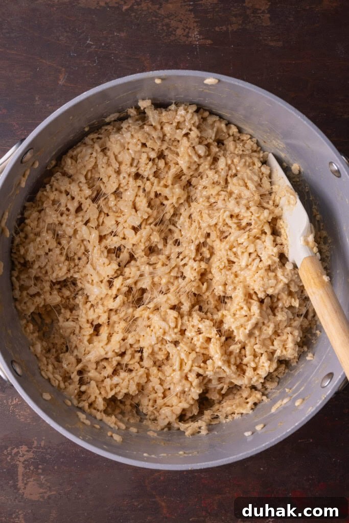 Using a spatula to mix rice krispie treats with melted marshmallows, peanut butter, and butter in a large pot. 
