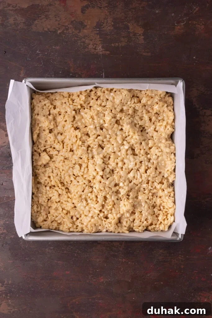 Smoothing out peanut butter rice krispies treats into a lined pan.