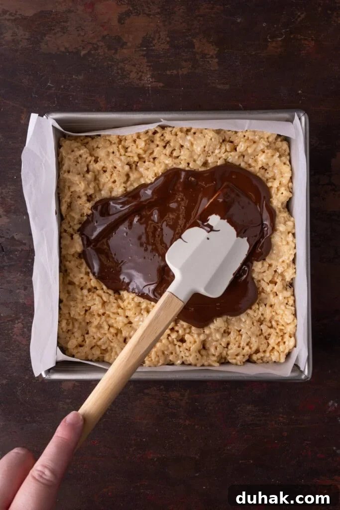 Smoothing out melted chocolate in an even layer on top of peanut butter rice krispies treats.