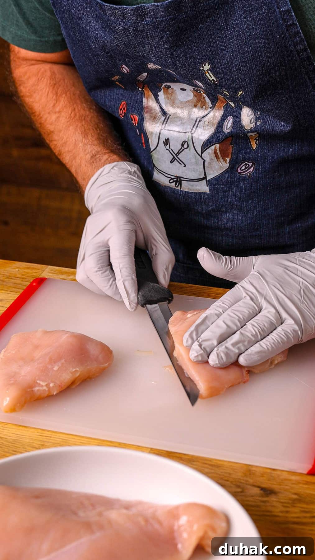 Chicken breasts getting trimmed on a cutting board.