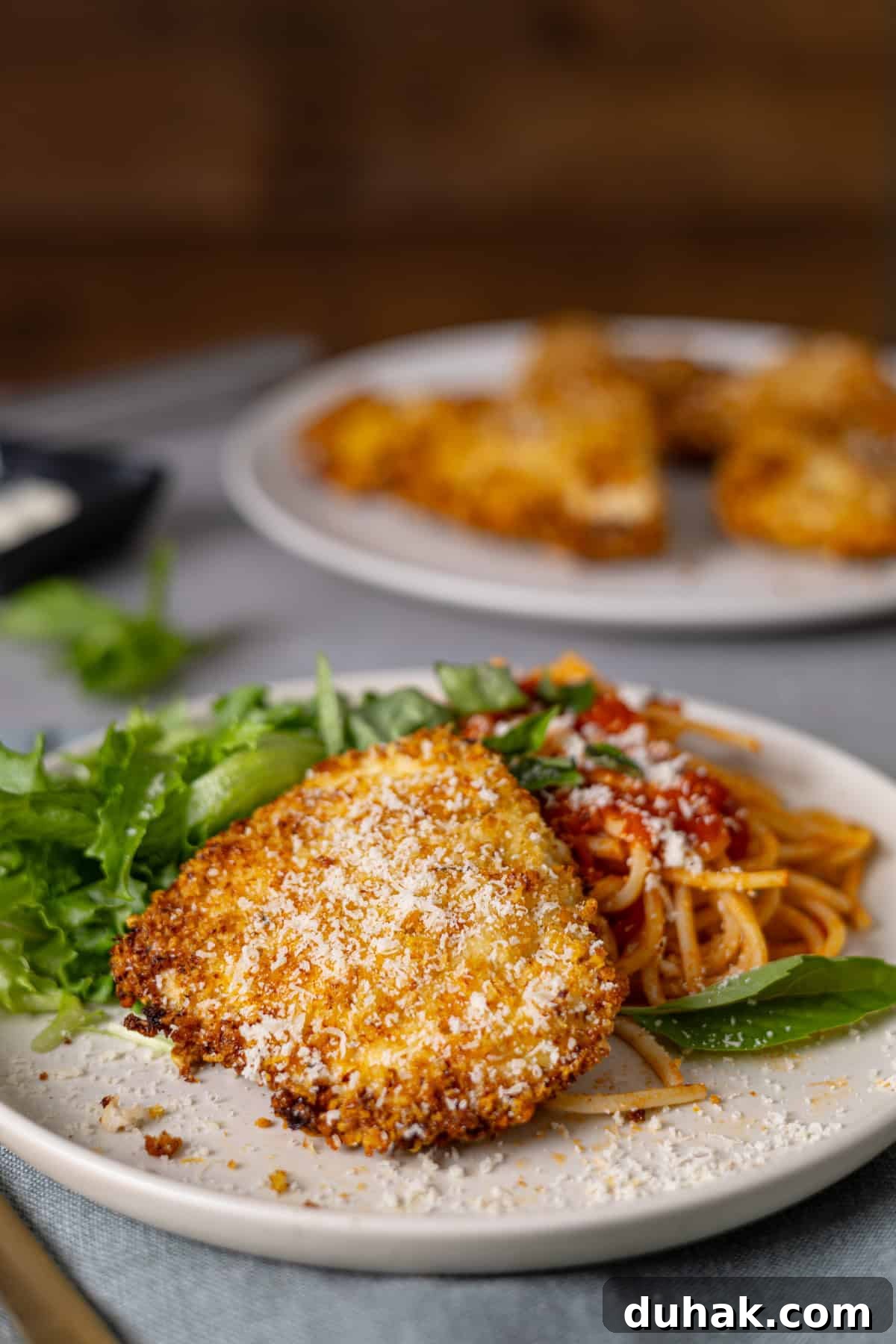 A closeup of crispy air fryer parmesan chicken with pasta, sauce, and salad on a plate.