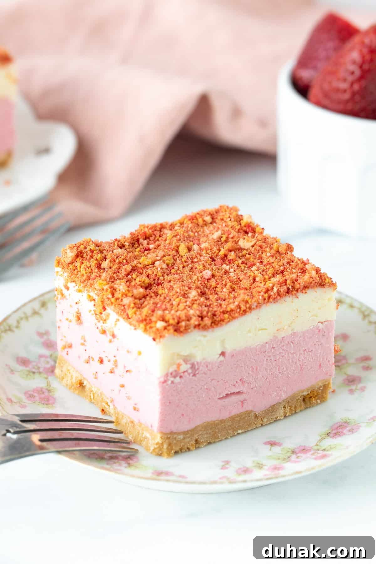 Slice of layered strawberry shortcake ice cream cake with strawberry crunch topping on a plate.