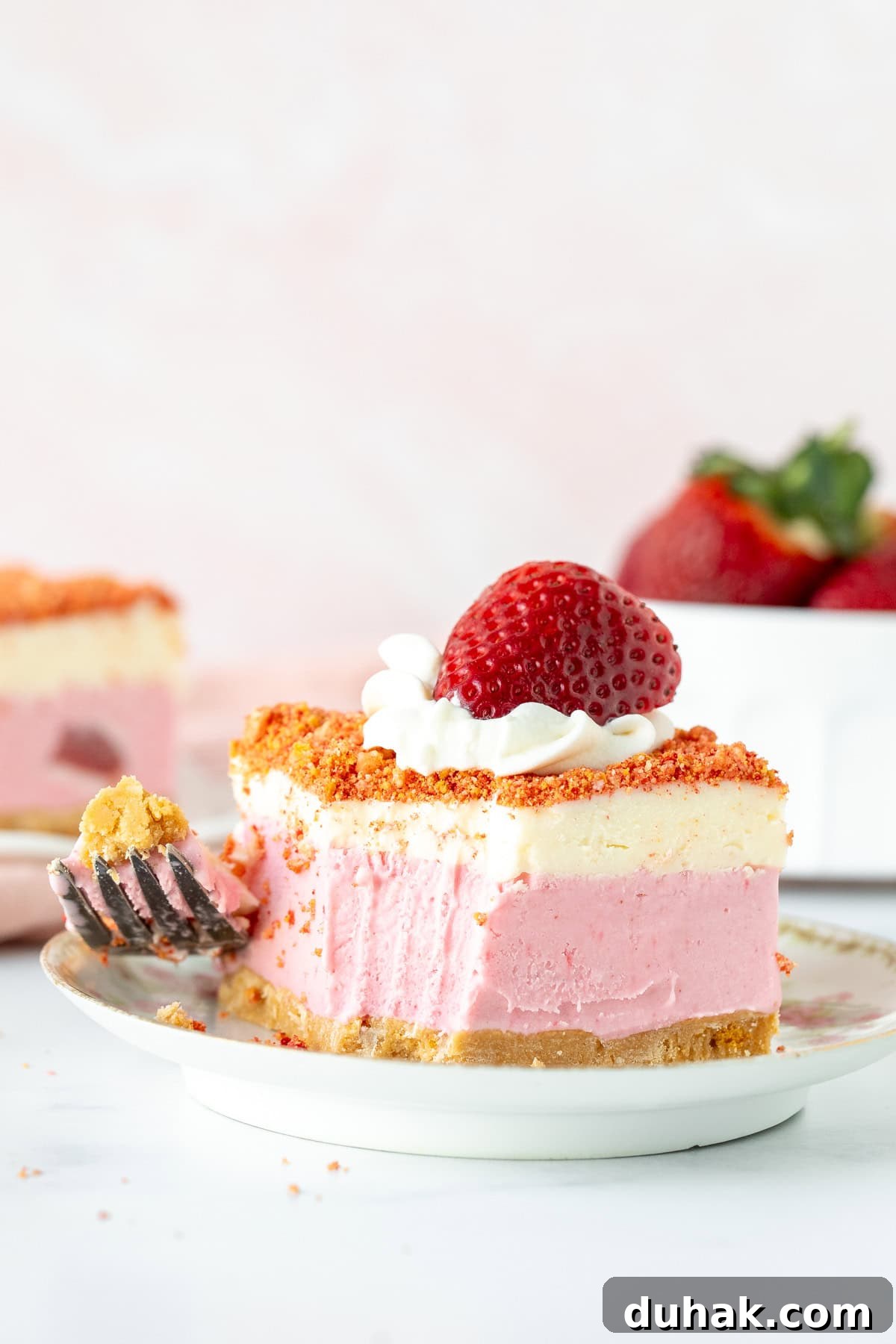 Slice of strawberry crunch ice cream cake on a plate with a bite taken out.