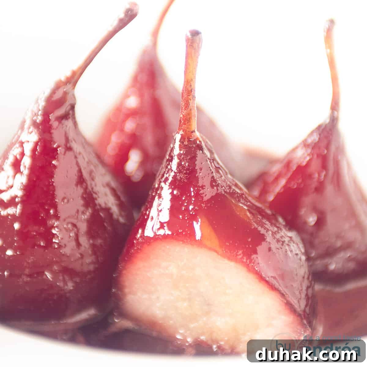 French Port-Poached Pears Recipe — Classic Dessert in Minutes 6 Four poached pears on a white plate. One pear is a slice cut off.