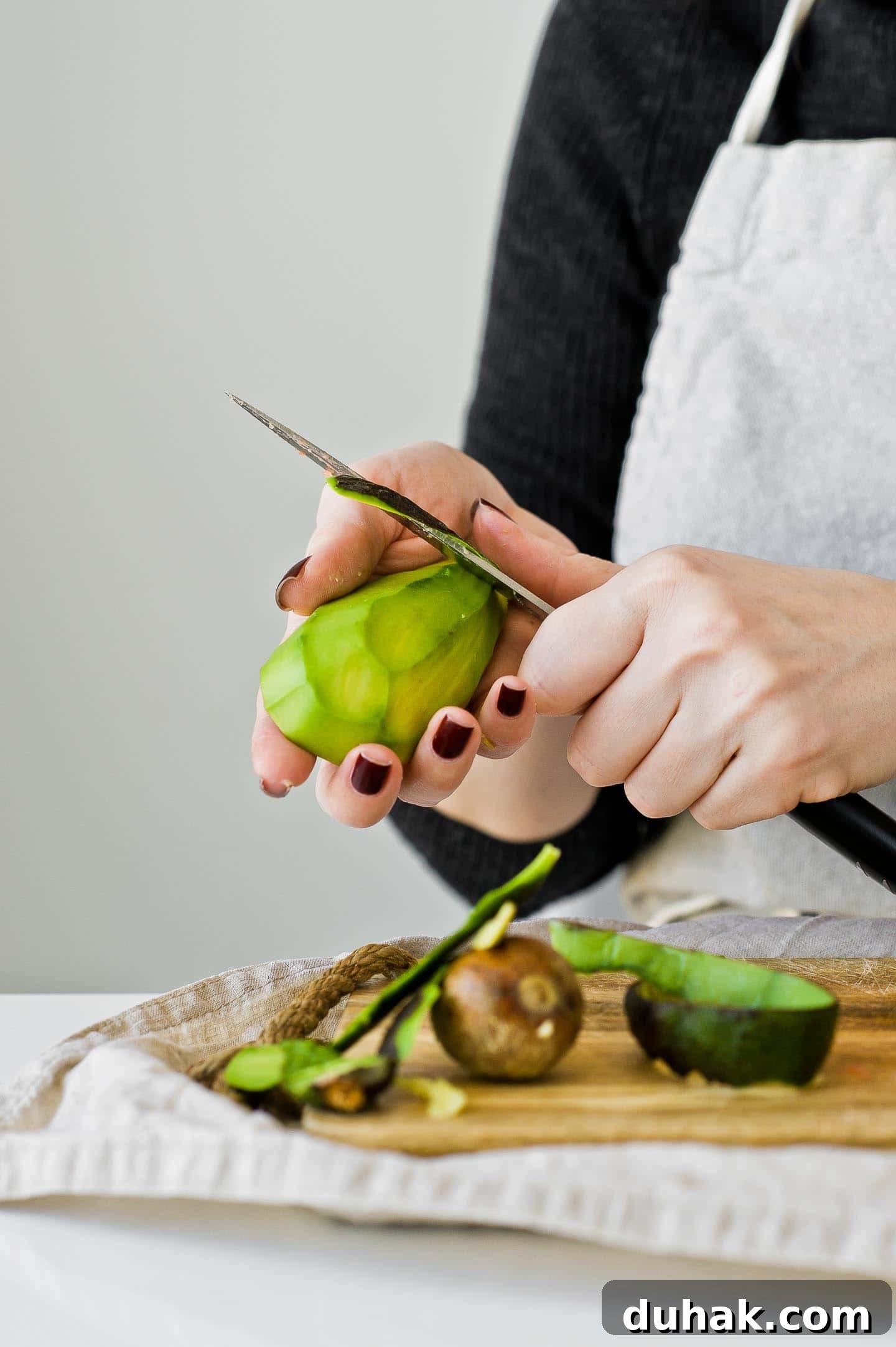Refreshing Nutrient-Packed Green Smoothie Recipe for Energy 3 Woman is peeling an avocado with a knife.