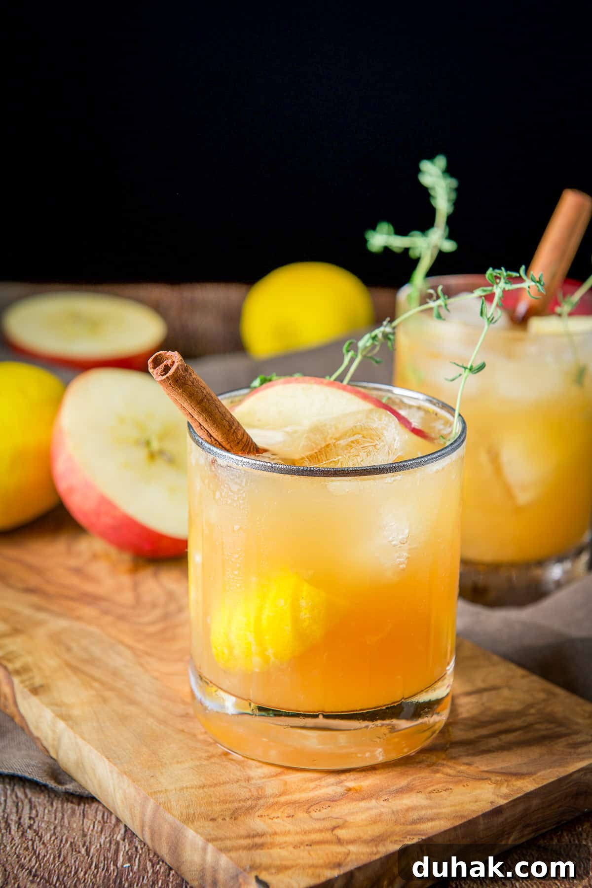 Apple Cider Bourbon Smash Cocktail Recipe 7 two glasses with the apple cider bourbon smash with apples, lemon and cinnamon sticks in them