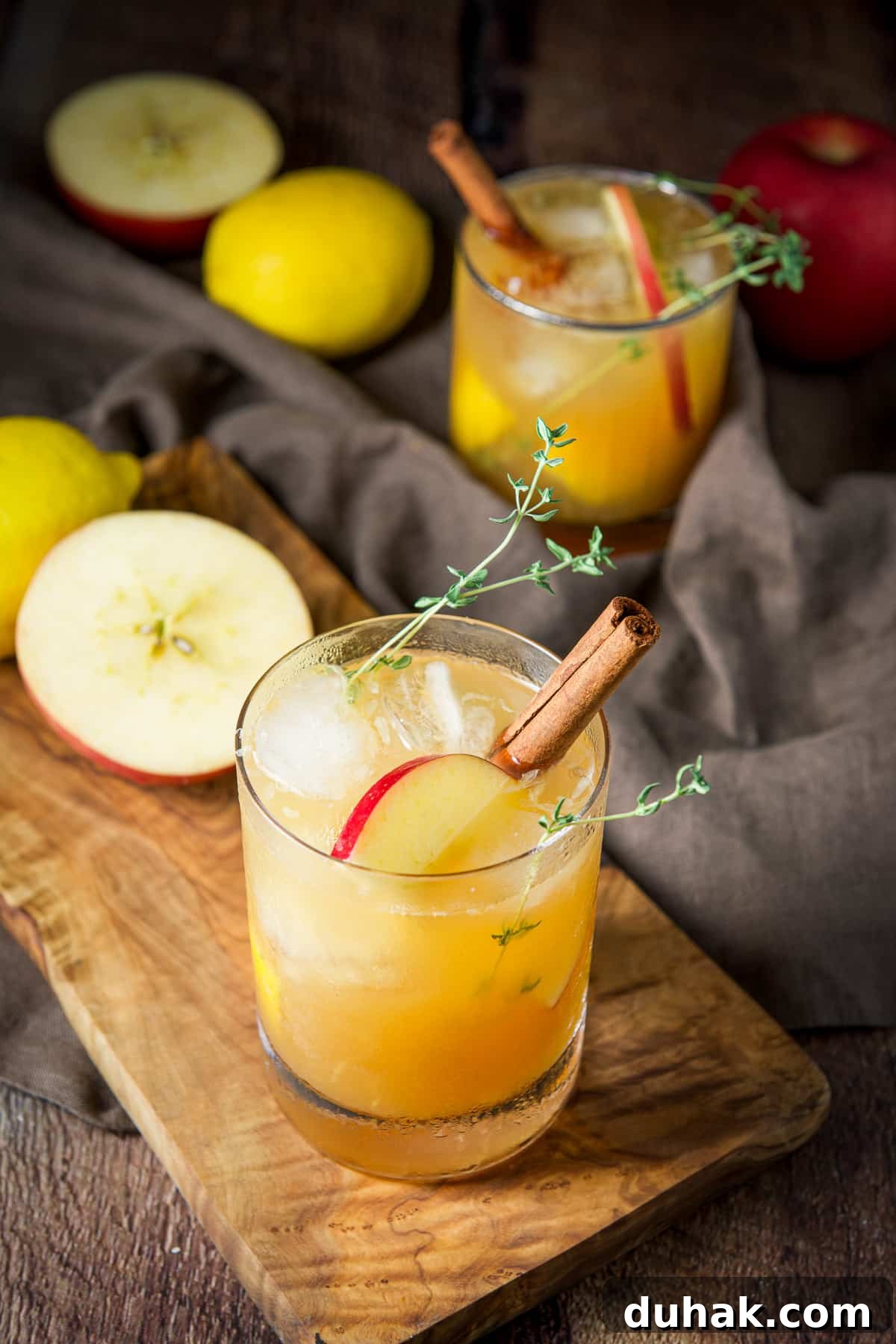 Apple Cider Bourbon Smash Cocktail Recipe 9 A glass on a wooden board filled with the apple bourbon smash with more apples and lemons