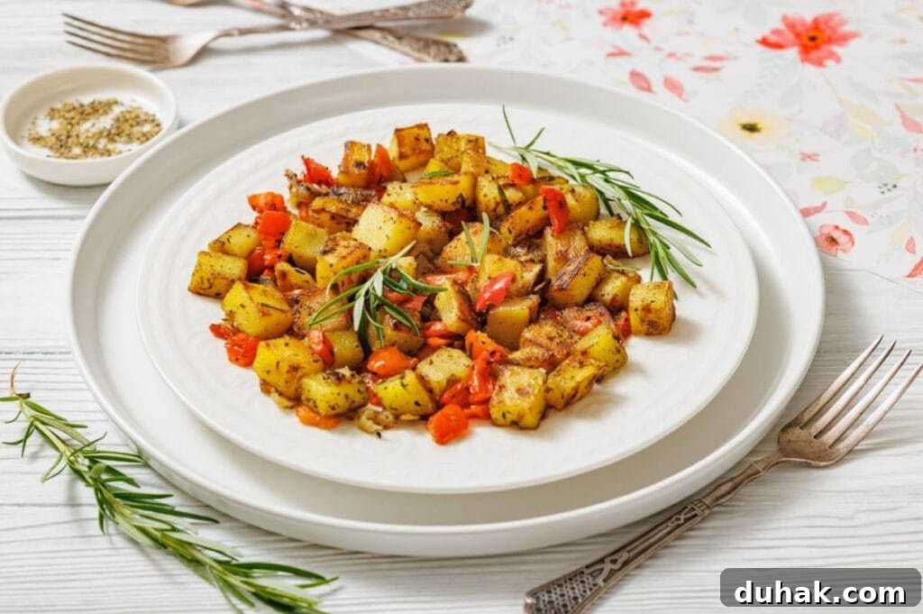 37 Comfort Food Recipes That Keep Reappearing on Menus 14 A white plate with Skillet Fried Potatoes garnished with rosemary sits on a white table with cutlery and a small bowl of pepper on the side.