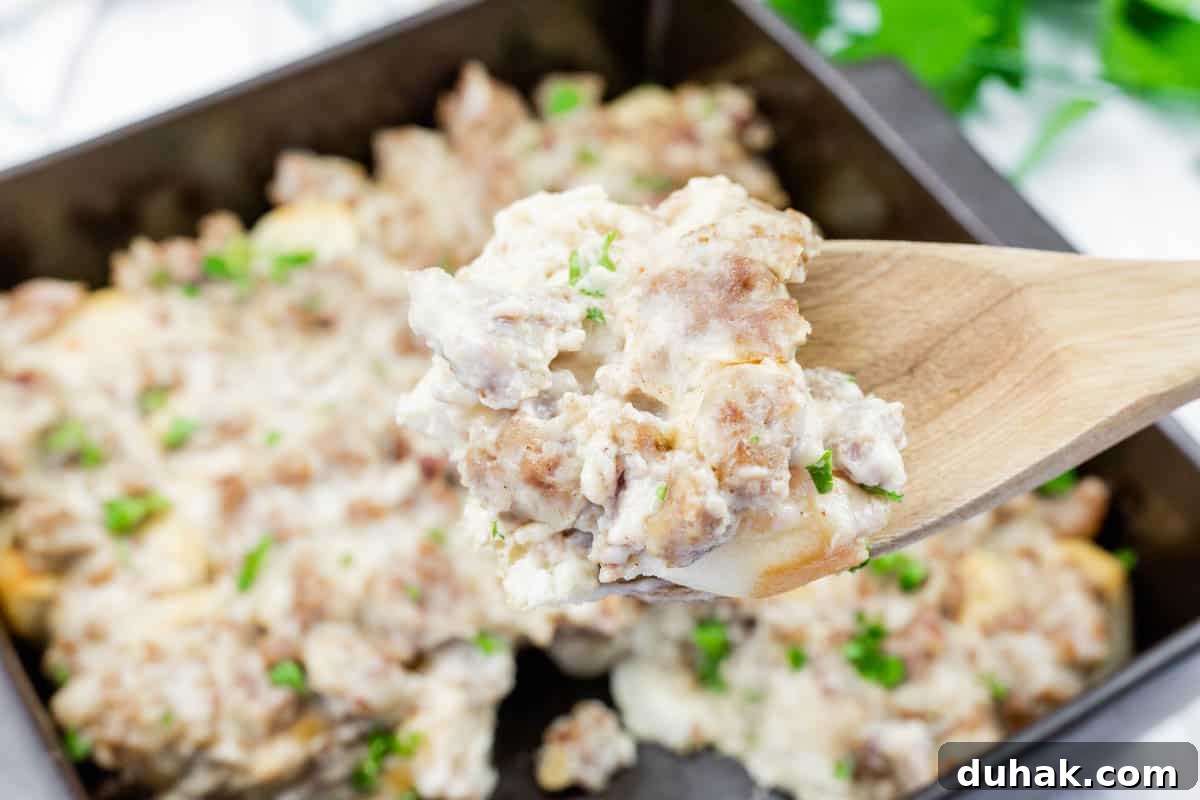 37 Comfort Food Recipes That Keep Reappearing on Menus 15 A wooden spoon holds a serving of biscuits and gravy with sausage, over a baking dish filled with the same dish, garnished with chopped herbs.