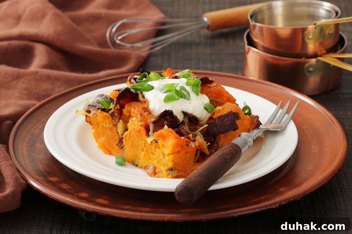 37 Comfort Food Recipes That Keep Reappearing on Menus 17 A white plate with loaded sweet potato casserole topped with sour cream, bacon, cheese, and green onions, set on a brown charger plate with a fork and cooking utensils in the background.