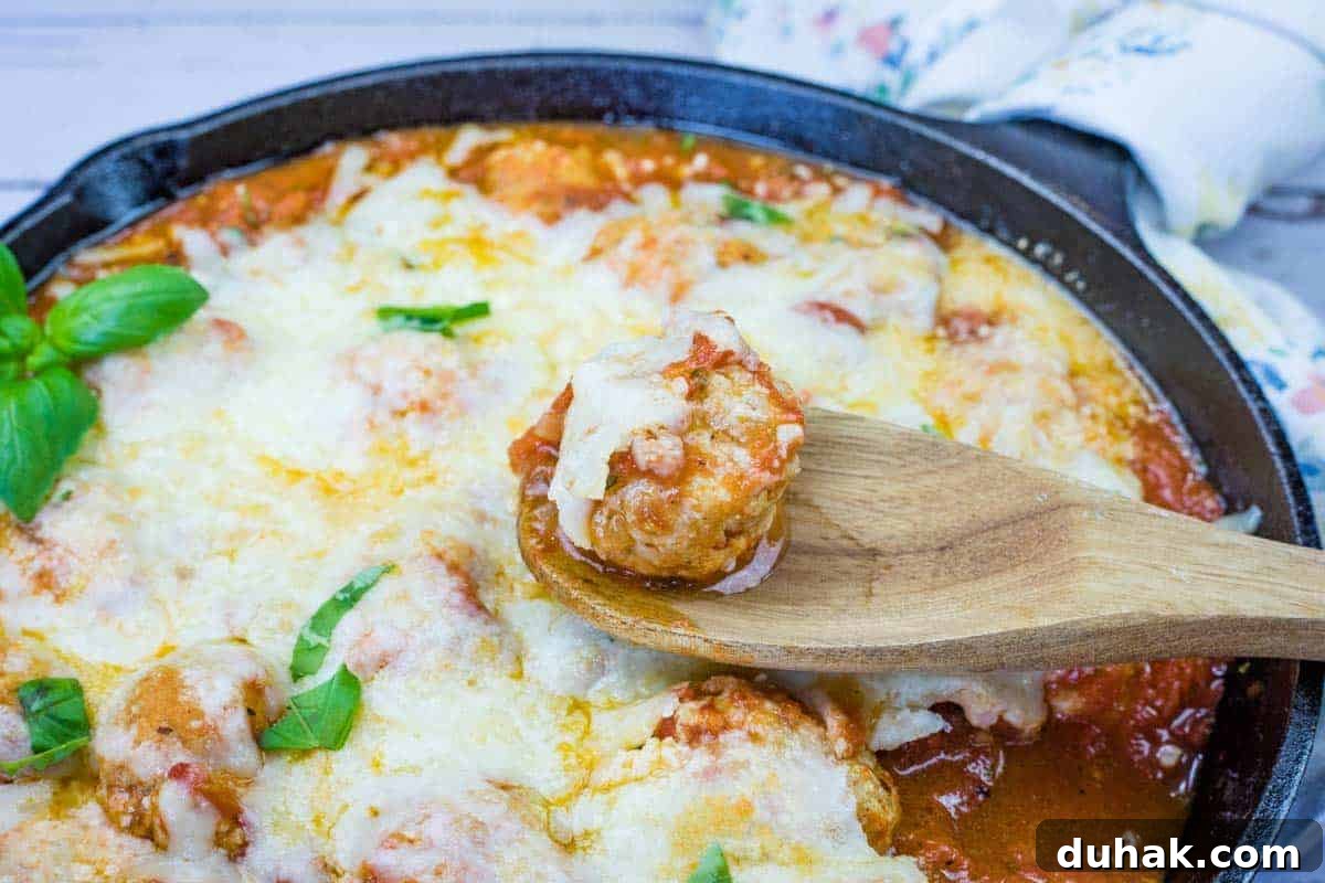 37 Comfort Food Recipes That Keep Reappearing on Menus 20 A wooden spoon holds a Chicken Parmesan Meatball over a skillet filled with meatballs.