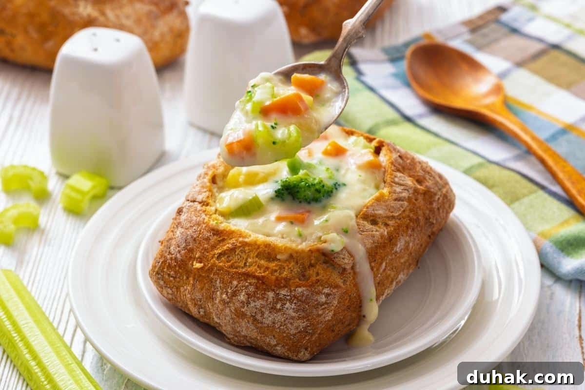 37 Comfort Food Recipes That Keep Reappearing on Menus 25 A bread bowl filled with creamy vegetable chowder, with a spoon scooping soup out; salt and pepper shakers, celery, and a wooden spoon are nearby.