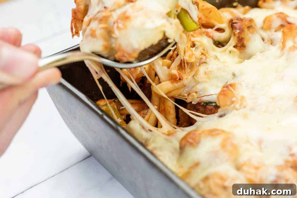 37 Comfort Food Recipes That Keep Reappearing on Menus 26 A hand uses a spoon to serve Easy Cheesy Meatball Casserole from a rectangular baking dish, with melted cheese stretching from the dish.