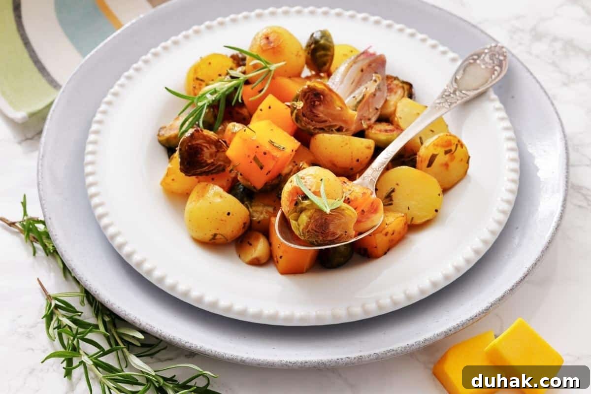 37 Comfort Food Recipes That Keep Reappearing on Menus 29 A plate of roasted vegetables including potatoes, Brussels sprouts, and squash, garnished with fresh herbs, with a serving spoon on a white plate.