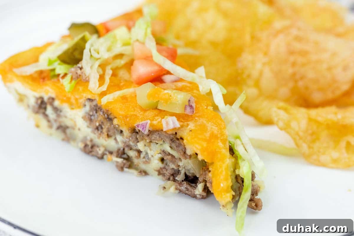 37 Comfort Food Recipes That Keep Reappearing on Menus 33 A slice of cheeseburger pie topped with shredded lettuce, diced tomato, onions, and pickles, served with potato chips on a white plate.