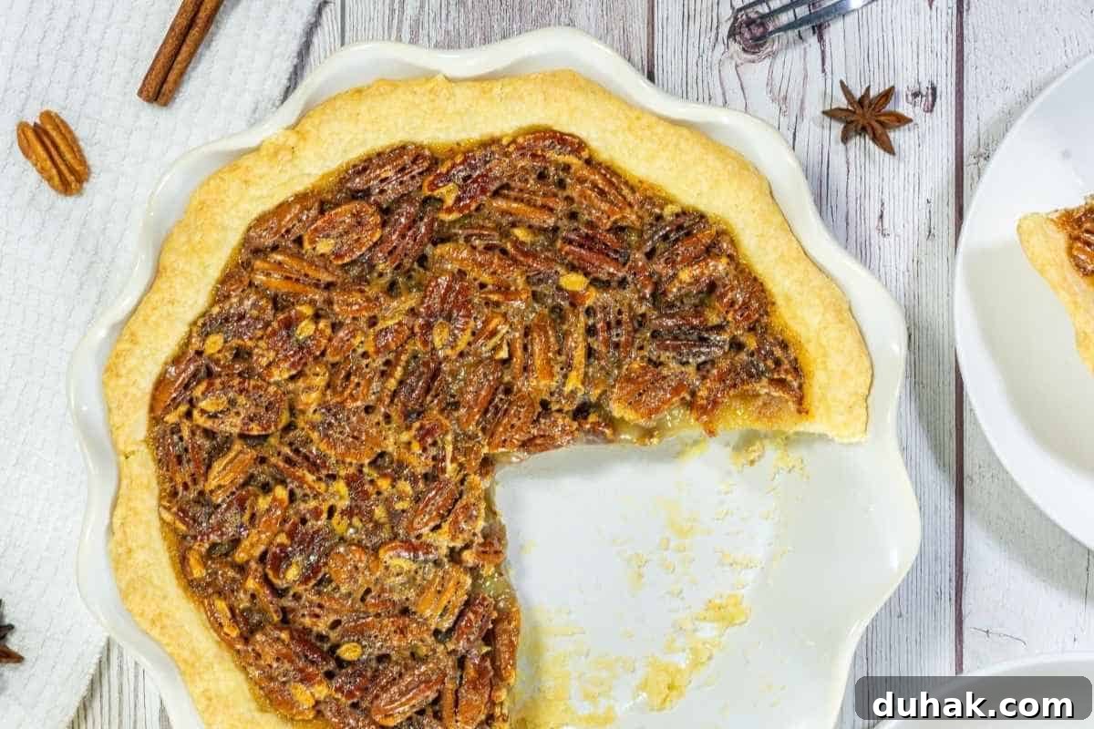 37 Comfort Food Recipes That Keep Reappearing on Menus 5 A pecan pie in a white dish with a large slice missing, shown on a light wooden surface.