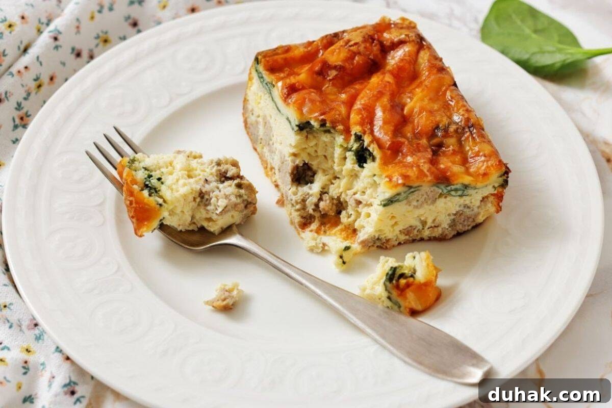 37 Comfort Food Recipes That Keep Reappearing on Menus 8 A slice of Sausage, Spinach, and egg casserole on a white plate, with a fork holding a bite-sized piece.