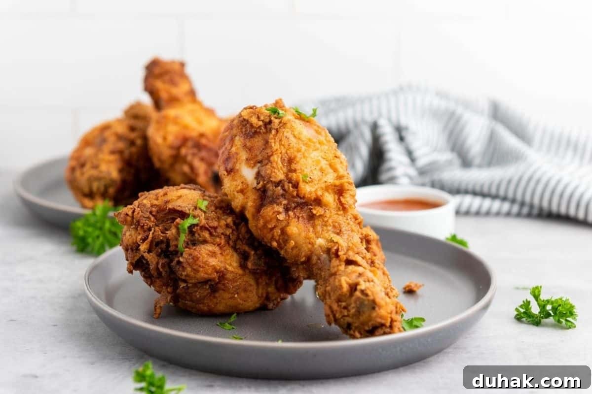37 Comfort Food Recipes That Keep Reappearing on Menus 10 A plate with pieces of fried chicken garnished with parsley, with a bowl of sauce and a striped cloth in the background.