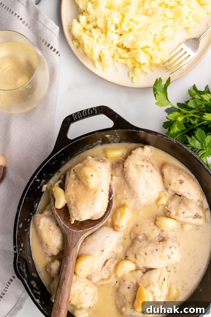 Pan-Seared Chicken Thighs with Creamy Garlic Gravy 2 chicken thighs in garlic gravy in a black skillet with a wooden spoon