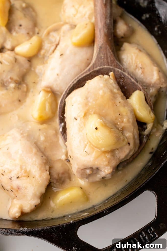 Pan-Seared Chicken Thighs with Creamy Garlic Gravy 3 a wooden spoon resting in a black skillet holding a chicken thigh in garlic gravy