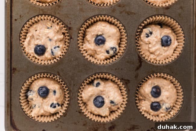 Unbaked blueberry muffin batter in a muffin tin.