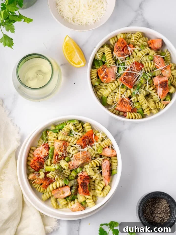 Creamy Salmon Pesto Pasta with Lemon Zest 17 two white bowls of salmon pesto pasta, glass of wine, lemon wedge, black pepper cellar