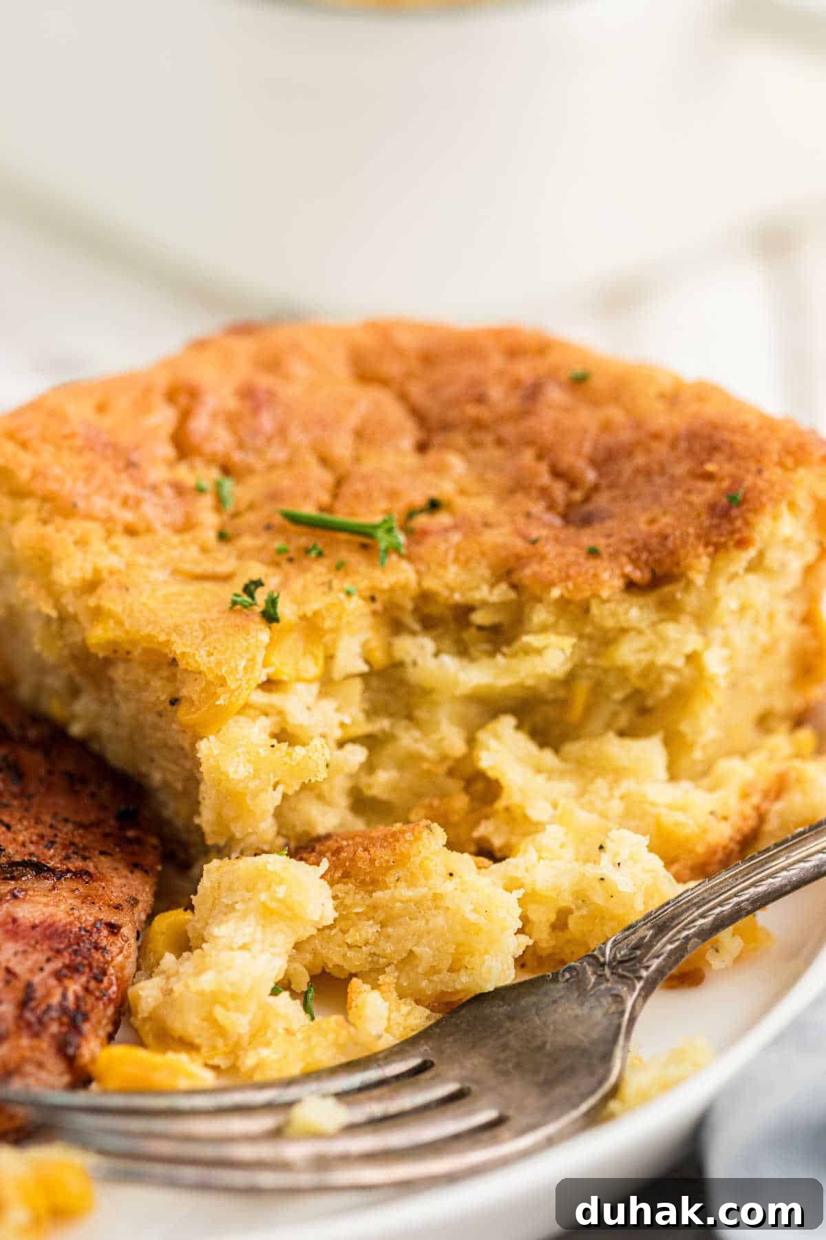 Close up of a dished up serving of cornbread pudding with a fork resting next to it.