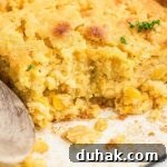 Close up shot of a dish of cornbread pudding with a wooden spoon resting.