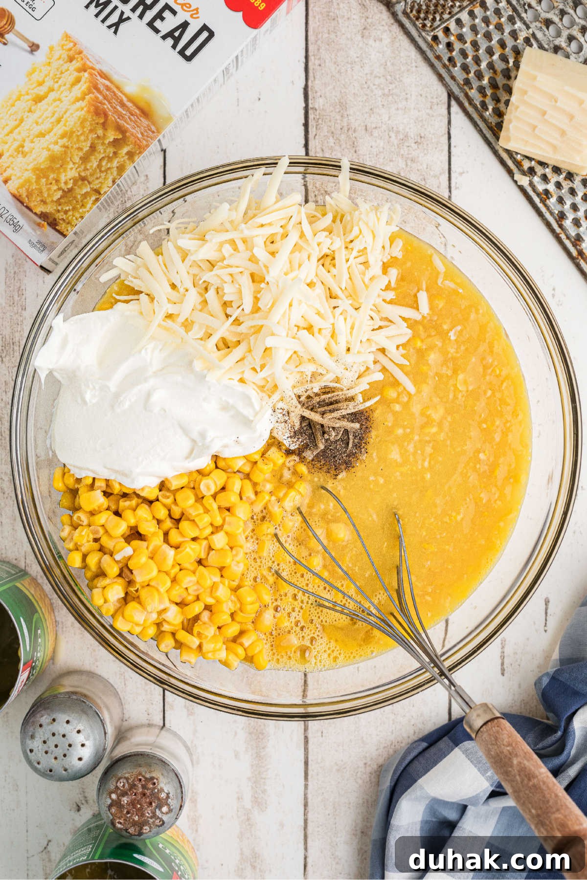 A mixing bowl filled with corn, cream style corn, sour cream and cheese.