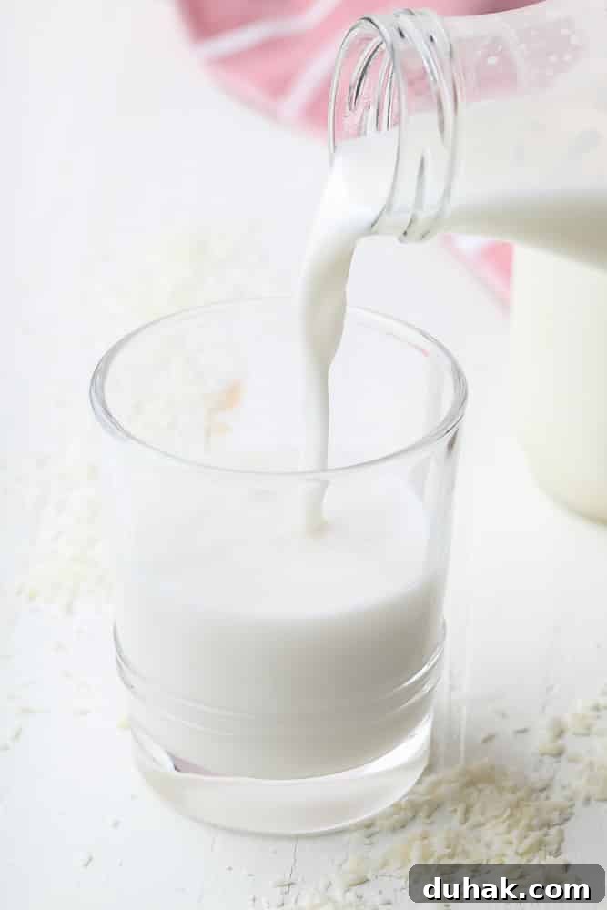 cup of milk being poured from a milk jug with coconut around it