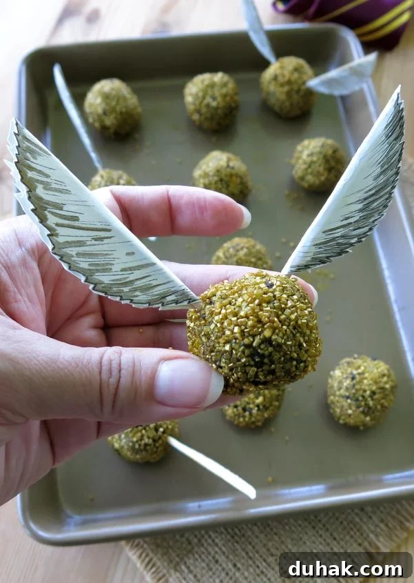 Hand holding an edible Harry Potter Golden Snitch Truffle with paper wings.